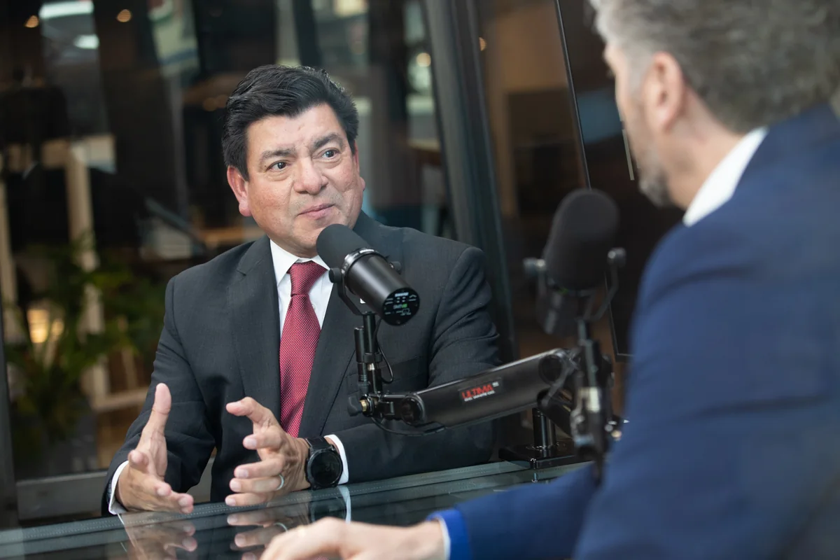 Two people speaking across microphones at a glass table in the studio.