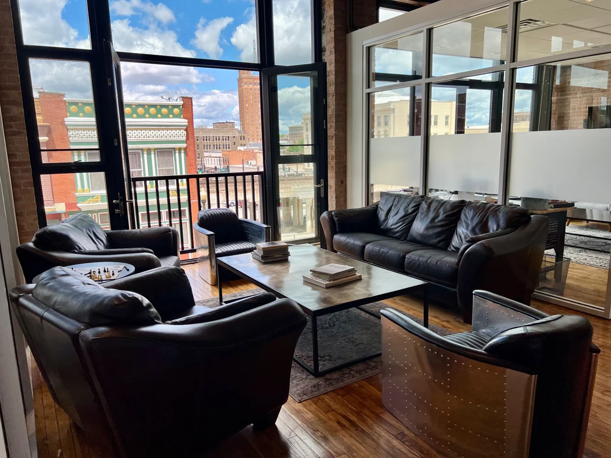 Sofas and chairs gathered around a table beside windows overlooking the city.